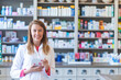 Smiling pharmacist chemist woman standing in pharmacy drugstore, looking at camera. Medicine, pharmacy, people, health care and pharmacology concept - happy young woman pharmacist