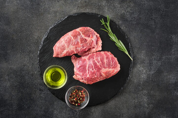 Wall Mural - Raw pork cheeks meat on a dark gray surface with rosemary and spices. Top view. Food background