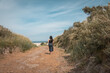 Young girl (woman) going for a walk in the dunes and sand beach on the Northsea coast of the german island Juist. Blue clouded sky and bushes of grass. Perfect summer trip.