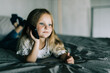 © F8  \ Suport Ukraine - Happy little girl talking on smartphone, looking aside while sitting on bed