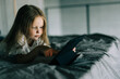 © F8  \ Suport Ukraine - Little girl lying on bed look at screen of tablet at home