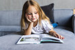 © F8  \ Suport Ukraine - Cute little small girl reading book on sofa at home