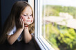 © F8  \ Suport Ukraine - Beautiful little girl smiling and watching out the window. A child looks out the window. Portrait of cheerful kid lies at windowsill.
