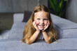 © F8  \ Suport Ukraine - Little girl having fun at home. Happy smile on the childs face. The child woke up after the day. Little girl lying on her stomach on the couch