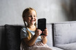 © F8  \ Suport Ukraine - Little small girl sitting on the couch in living room texting on smartphone.