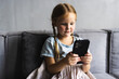 © F8  \ Suport Ukraine - Little small girl sitting on the couch in living room texting on smartphone.