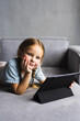 © F8  \ Suport Ukraine - cute little happy girl smile lying down on sofa using looking digital tablet pad in the living room at home. family activity concept.
