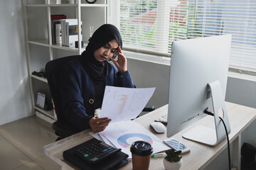 Muslim woman wearing hijab sitting on office chair, looking at the sheet with serious thinking about how to solve her company problems. Concept of stress at work