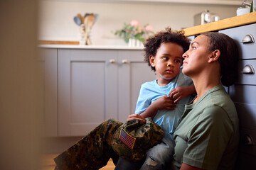 Young Son Comforts Depressed Mother Suffering With PTSD Sitting On Floor On Home Leave