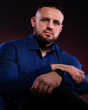 © oleg_ermak - Portrait of confident handsome man in blue shirt with his hands crossed a black watch on his arm. Posing in studio on dark red background