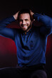 © oleg_ermak - Surprised and glad man in blue shirt, hold hands on his head. Handsome Posing in studio on dark red background