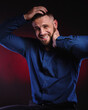 © oleg_ermak - Surprised and glad man in blue shirt, hold hands on his head. Handsome Posing in studio on dark red background