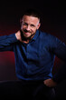 © oleg_ermak - Surprised and glad man in blue shirt, hold hands on his head. Handsome Posing in studio on dark red background