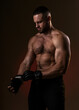 © oleg_ermak - Studio portrait of fighting muscular man puts on fighting gloves posing on dark background. The concept of mixed martial arts. Brutal bodybuilder energy and power boxing.