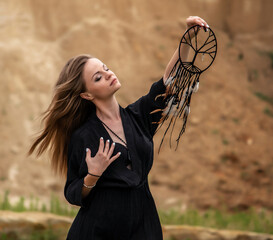 shaman girl in a black dress with a dream catcher on the background of mountains