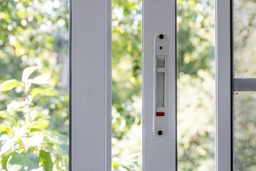 Close-up of a double-glazed balcony frame with a latch and fastening for safe ventilation. Single-sided window handle. House door and window repair concept