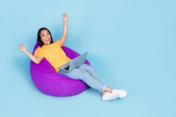 Poster - Full size photo of adorable young lady korean win online lottery laptop beanbag wear trendy yellow outfit isolated on blue color background