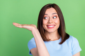 Wall Mural - photo of cheerful pretty girl look arm palm hold demonstrate empty space isolated on green color bac