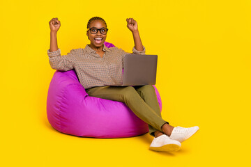 Wall Mural - Photo of cute lucky woman wear plaid shirt sitting beanbag reading modern device rising fists isolated yellow color background