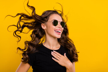 Wall Mural - Photo of impressed pretty young woman wear black outfit dark eyeglasses air blowing looking empty space isolated yellow color background