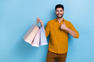Wall Mural - Photo of hooray beard millennial guy hold bags thumb up wear brown shirt isolated on blue color background