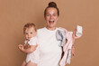 © sementsova321 - Extremely happy young mother with bun hairstyle holding her toddler daughter and screaming happily, rejoicing, hearing good news, posing isolated over brown background.