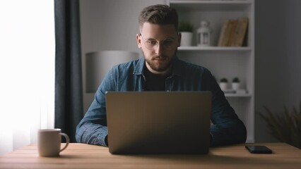 Handsome bearded man typing on laptop, young coder writing code, home office with light interior