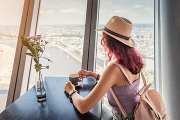 Wall Mural - Happy girl drinking coffee in a cafe and admires out of the window on the observation deck of the TV Tower in Dusseldorf. Great viewpoint for tourists in Germany