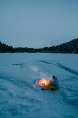 Poster - Person sitting at a bonfire and getting warmed in the cold snow-covered field at dusk