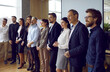 © Studio Romantic - Professional business people of different ages take part in meeting or listen to speech of CEO company or corporate and look in one direction standing in row in conference room. Panoramic shot