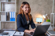 © amnaj - Happy young asian businesswoman sitting on her workplace in the office. Young woman working at laptop in the office.