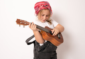 Poster - Cute little girl in denim clothing playing ukulele over white background. Happy vacation concept.