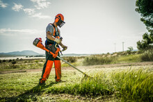 Backlit Side View Of A Man Removing Grass With A Trimmer
