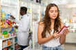 © JackF - Young woman who came to the pharmacy attentive chooses a hair care remedy, studying its components