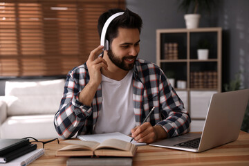 Wall Mural - Young man watching webinar at table in room