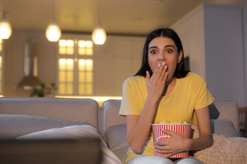 Wall Mural - Young woman watching movie with popcorn on sofa at night, space for text