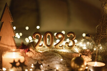 Happy New Year 2023. Number 2023 Made By Candles On A Festive Sparkling Bokeh Background In The Dark. New Year Background With Sweaters, Garlands And New Year Decorations.