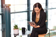 © feeling lucky - Portrait of confident young asian businesswoman researching and planning work with happy smiling face while sitting and using tablet at business meeting in modern office building and city background