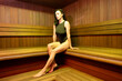 Beautiful adult woman in black swimsuit rests in finnish sauna, having spa procedures at luxury resort