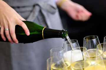 closeup of a champagne bottle pooring champagne into a champagne flute against a blurred person at a party