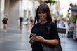 © Adam Radosavljevic - Beautiful smiling woman in black shirt texting on smartphone on street in city center