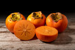 Ripe persimmon fruits one of them cut on weathered white wood with dark background
