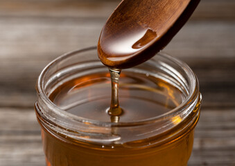 Wall Mural - Honey and wooden spoon in glass container on old wooden background.