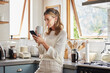 © Nina Lawrenson/peopleimages.com - Coffee, phone and senior woman in kitchen browsing social media, text message or online app at home. Relax, tea and reading news or mobile online web surfing with female from Canada on 5g smartphone