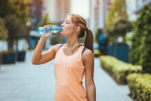 Photo Of Young Woman Drinking Water From Bottle. Caucasian Female Drinking Water After Exercises Or Sport. Beautiful Fitness Athlete Woman Wearing Hat Drinking Water After Work Out Exercising 