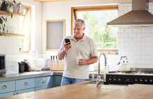 Senior Man, Morning Coffee And Phone Looking Happy While Reading Text Message, Online News Or Browsing Internet In Kitchen At Home. Male Using Messenger Or Social Media Mobile App In Australia House