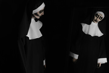 Scary devilish nun near mirror on black background. Halloween party look