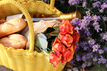 Wall Mural - Yellow wicker bag with beautiful roses, bottle of wine and baguettes near lavender flowers outdoors, above view