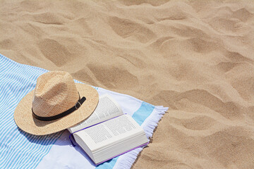 Poster - Beach towel with open book and straw hat on sand, space for text