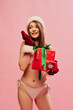 © master1305 - Portrait of young beautiful woman posing in swimsuit isolated over pink studio background. Lady Santa. Gifts